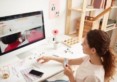 Young woman in tshirt sitting at table and entering number of credit card on website while buying goods on internet