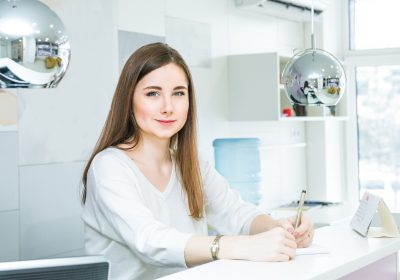 portrait-of-a-friendly-young-woman-looking-at-the-camera-writing-note-behind-the-reception-desk-