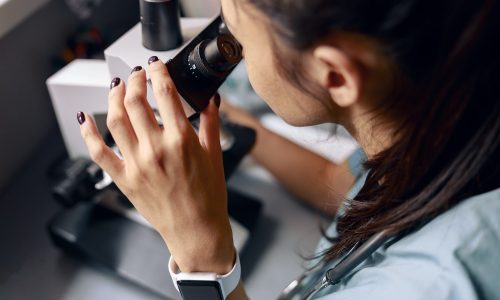 scientist-looks-into-microscope-researching-material-sample-at-table-in-laboratory