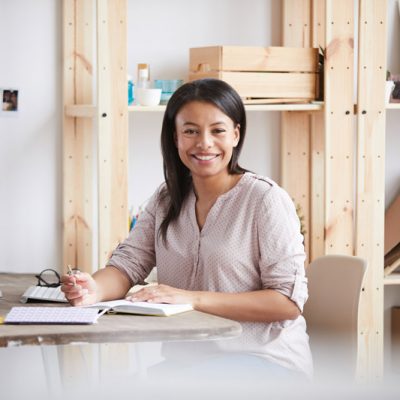 Portrait of young mixed race woman smiling happily while working or studying sitting at desk in home office, copy space